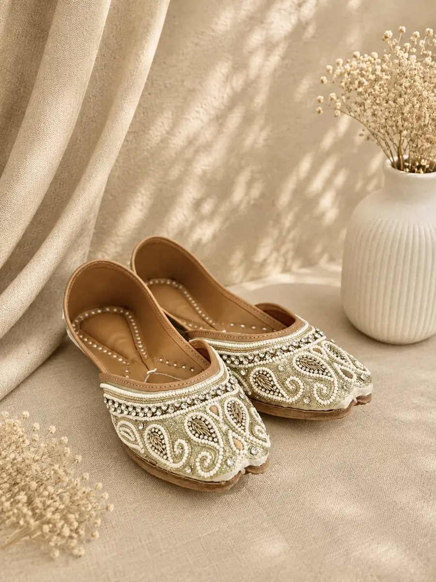 A pair of Ivory Grace juttis resting on cream fabric, seen from the side.