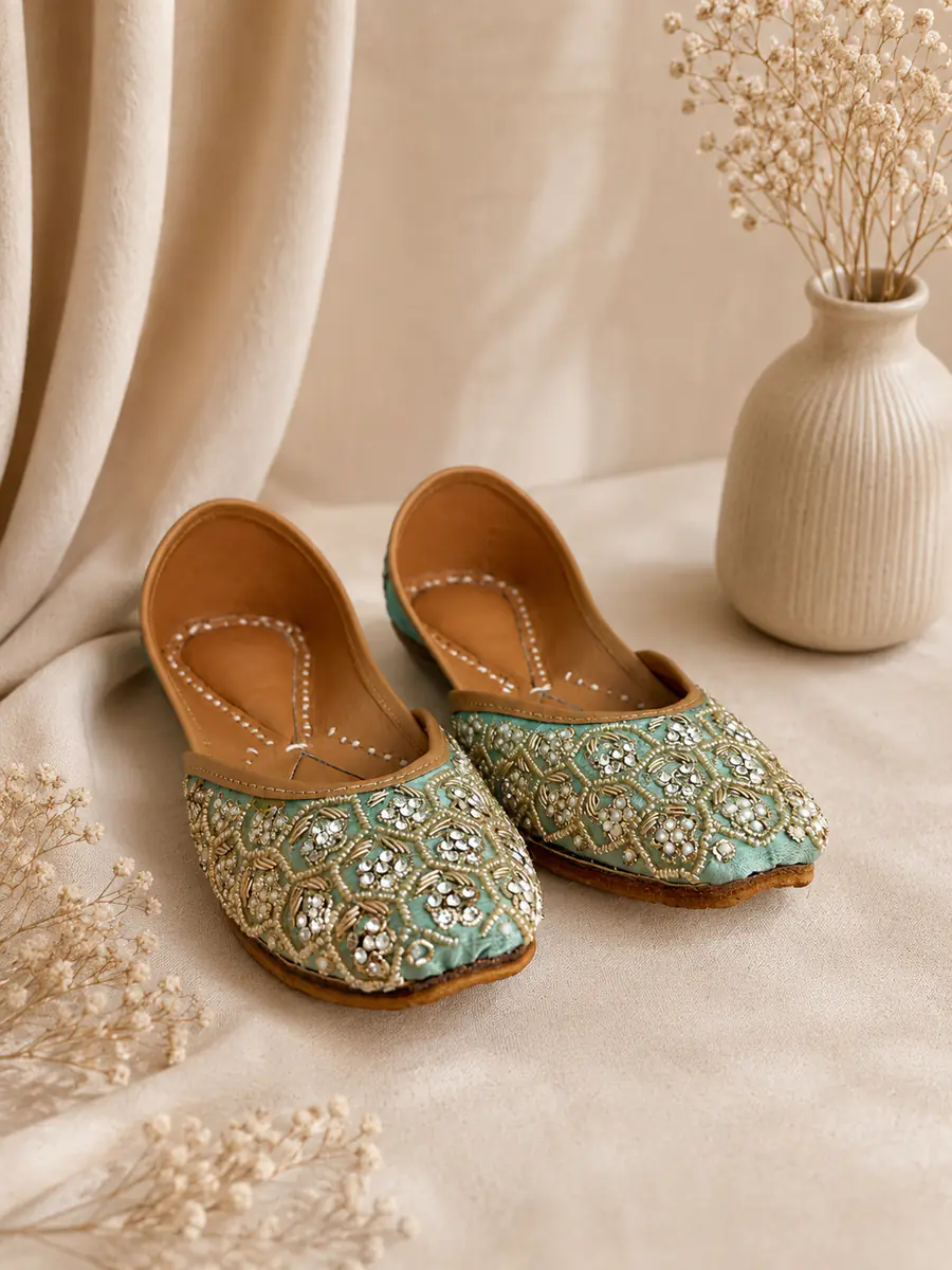 A pair of Jade Noor juttis resting on cream fabric, seen from the side.